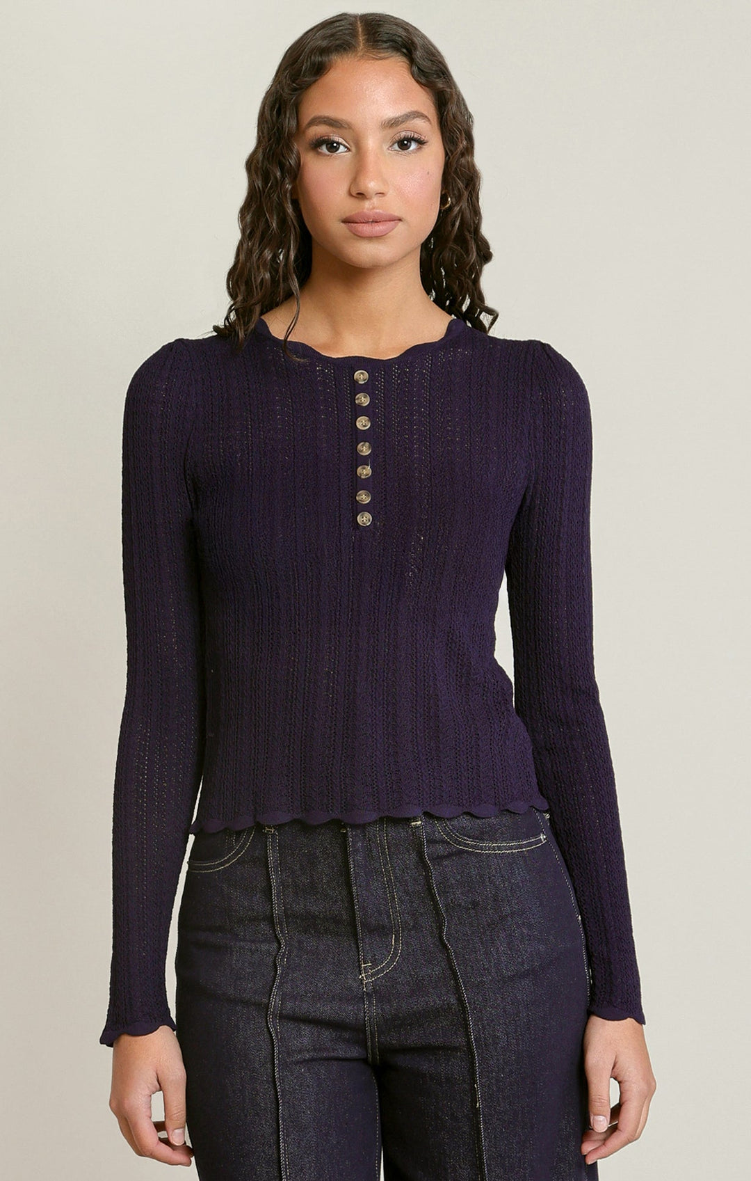 Woman wearing a dark purple long-sleeve top with buttons on a beige background