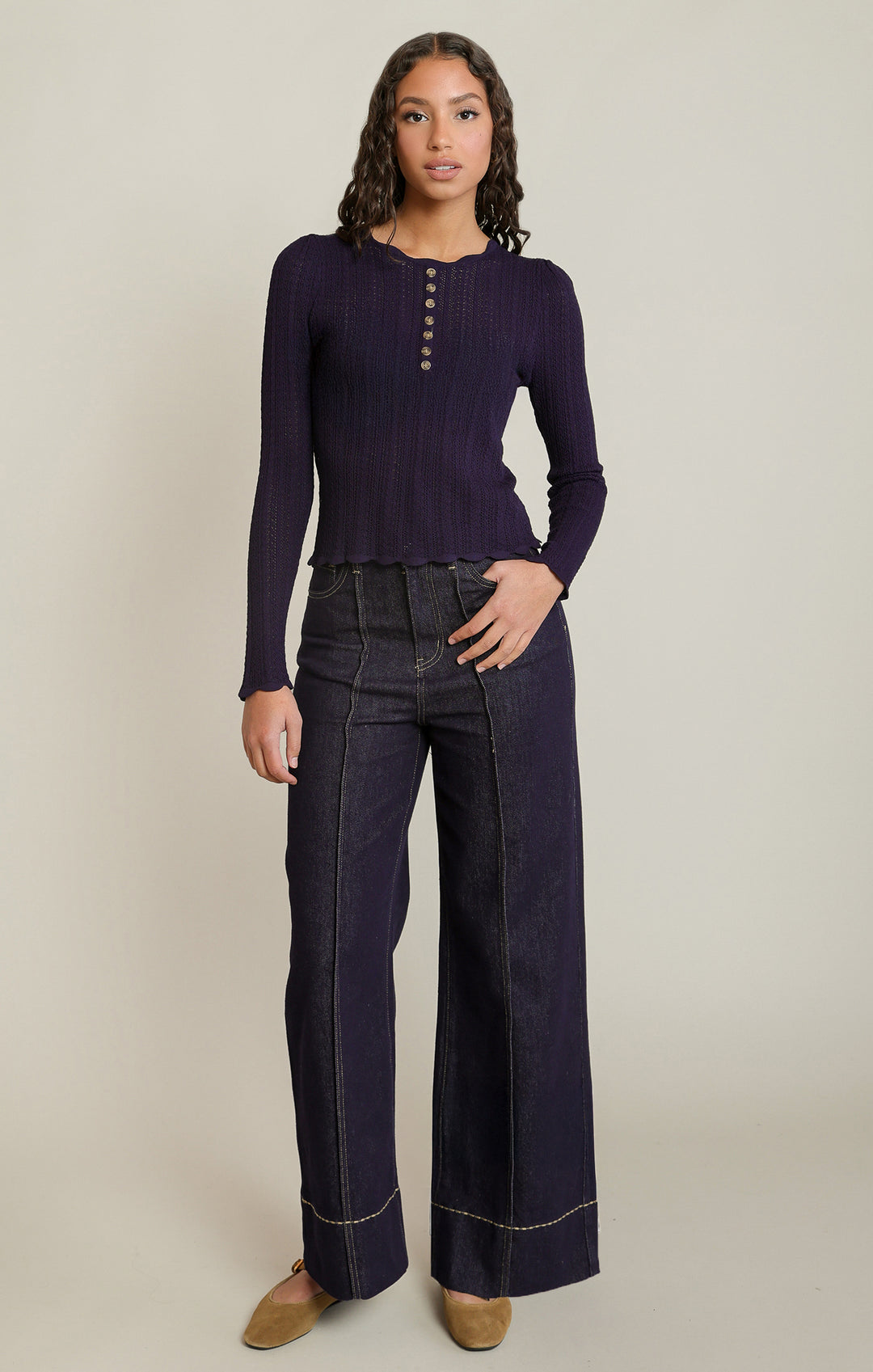 Woman wearing a purple long-sleeve top and dark blue wide-leg jeans on a beige background