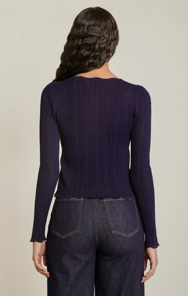 Person wearing a dark purple sweater and jeans on a beige background