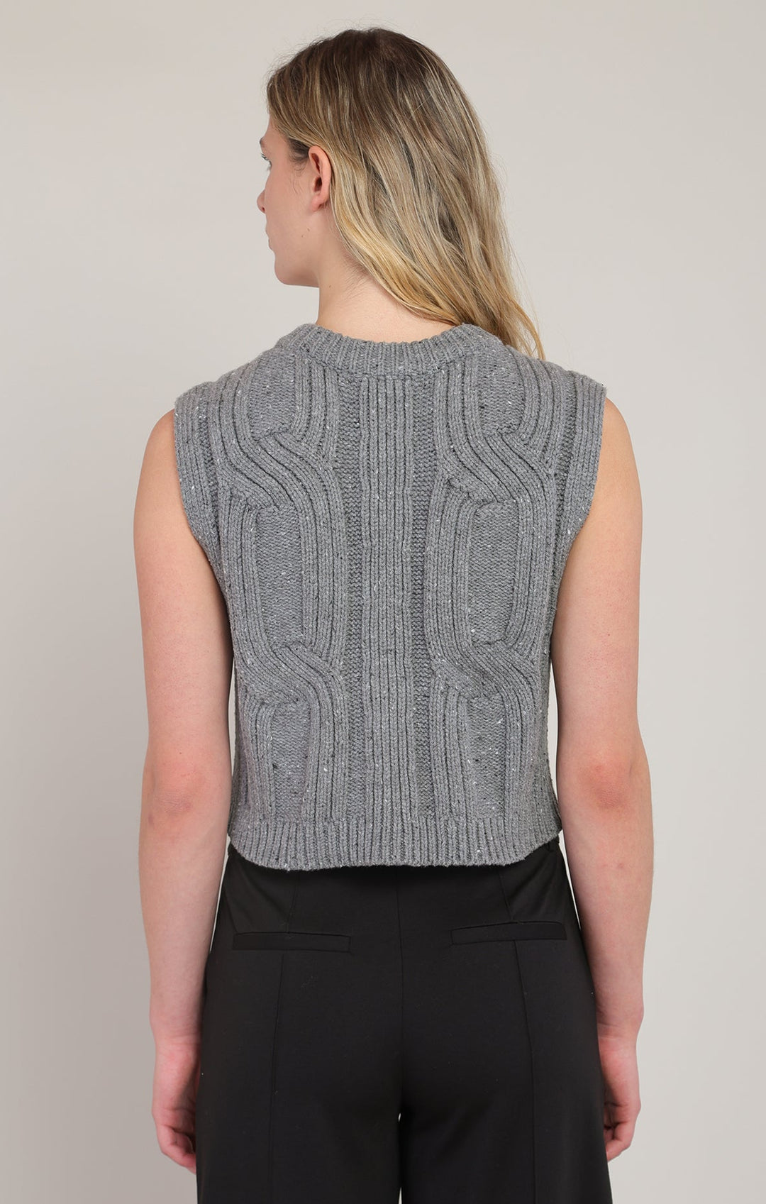 Person wearing a gray knitted vest against a plain background