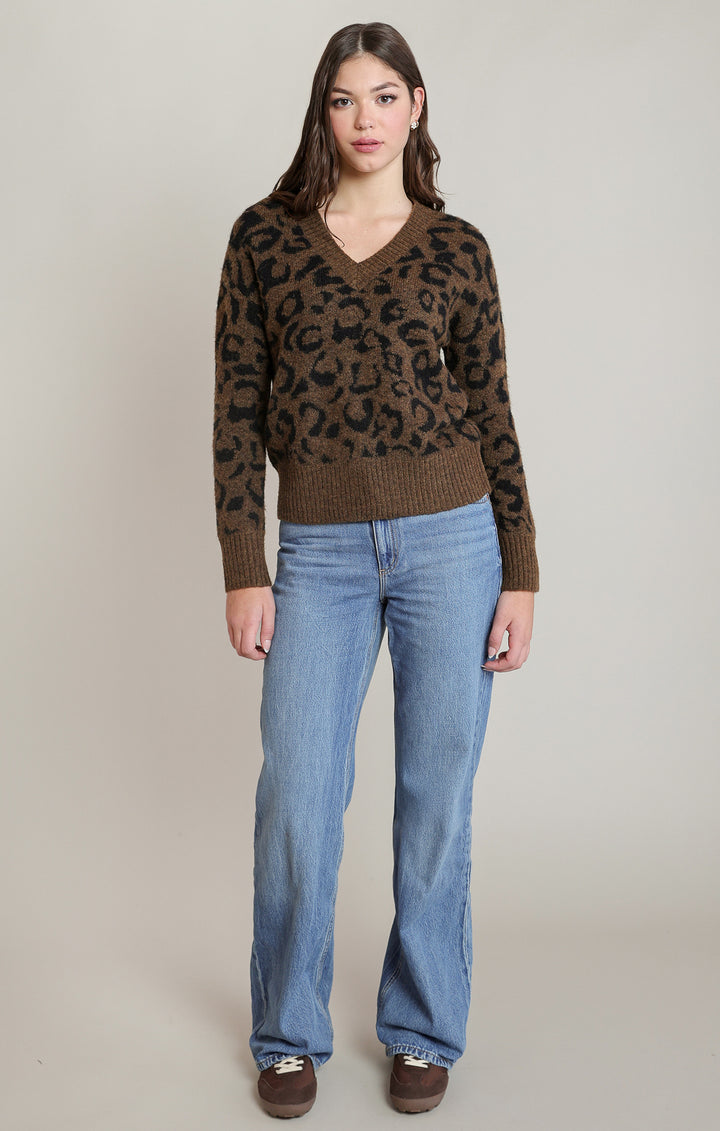 Woman wearing a brown leopard print sweater and blue jeans on a plain background