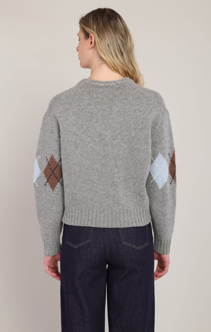 Person wearing a gray sweater with diamond pattern on sleeves against a plain background