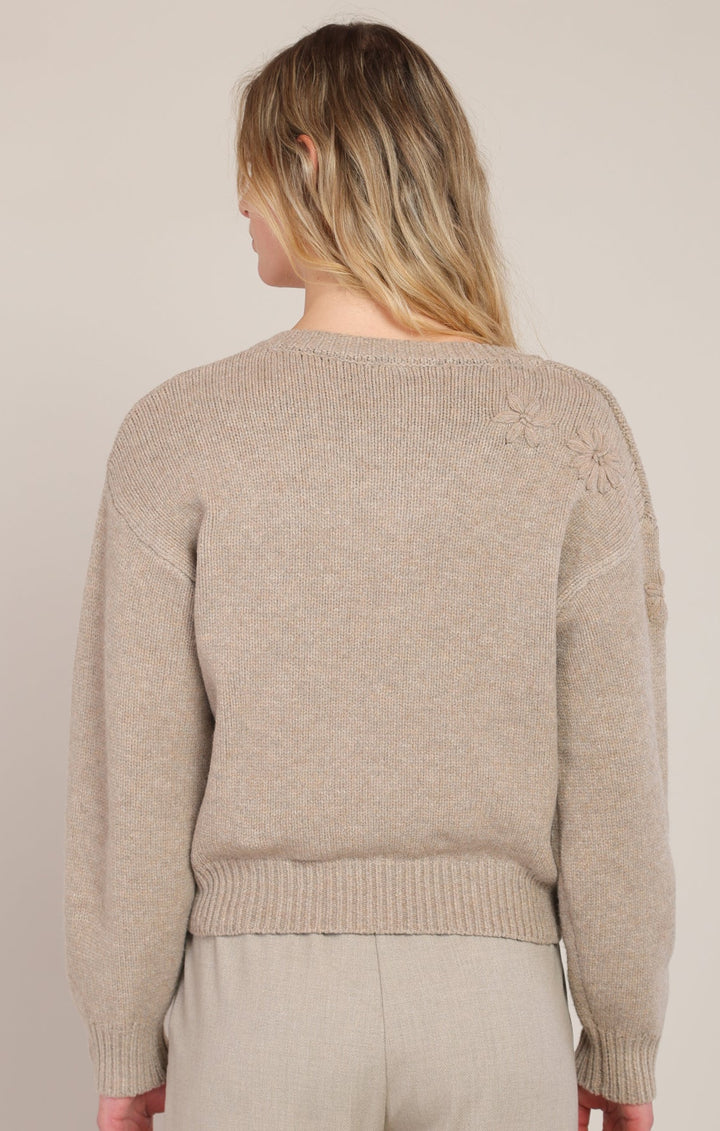 Person wearing a beige sweater and pants against a plain background