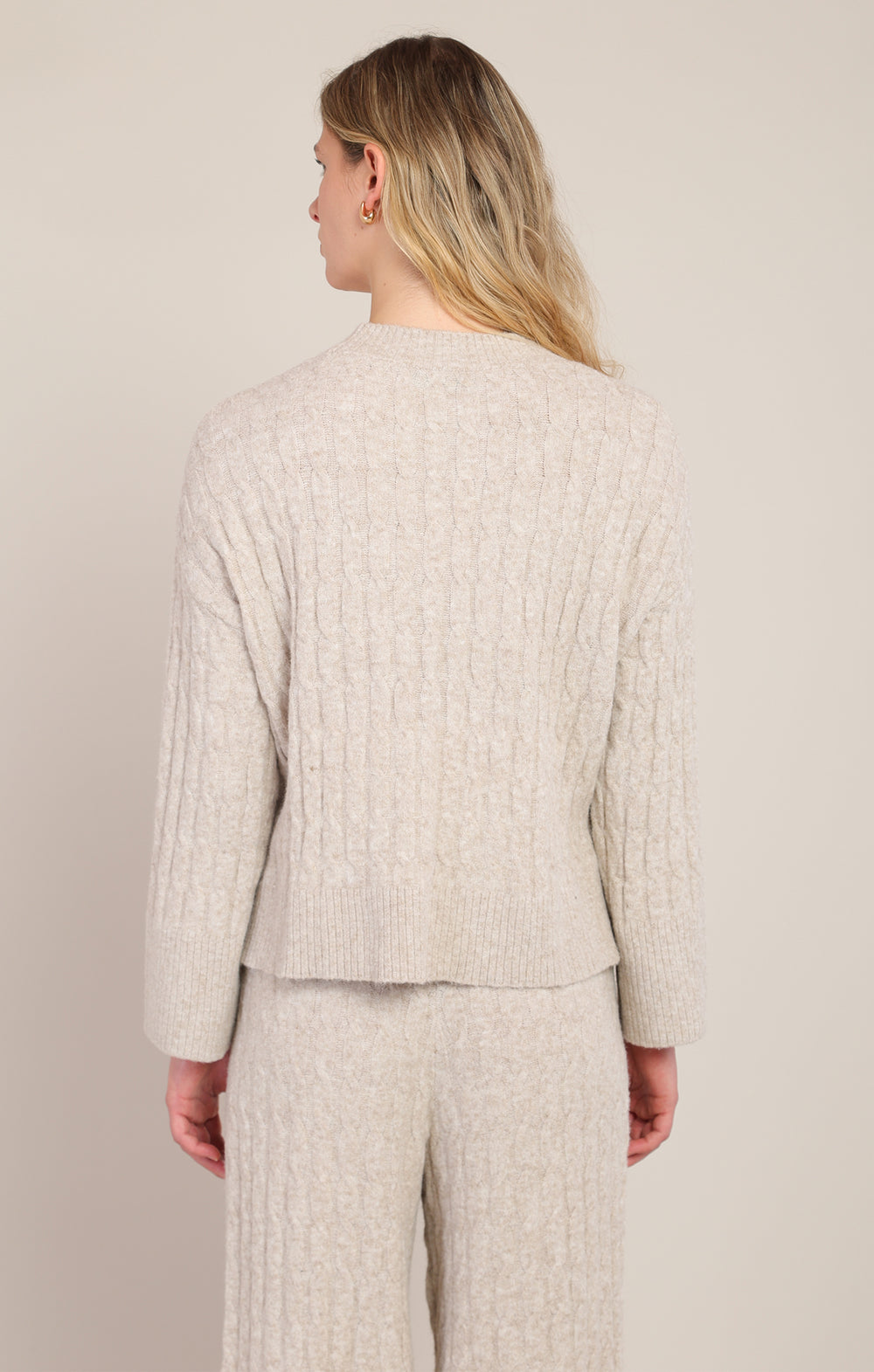 Woman wearing a beige textured suit against a plain background