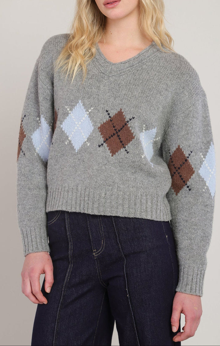 Woman wearing a gray sweater with argyle pattern against a plain background