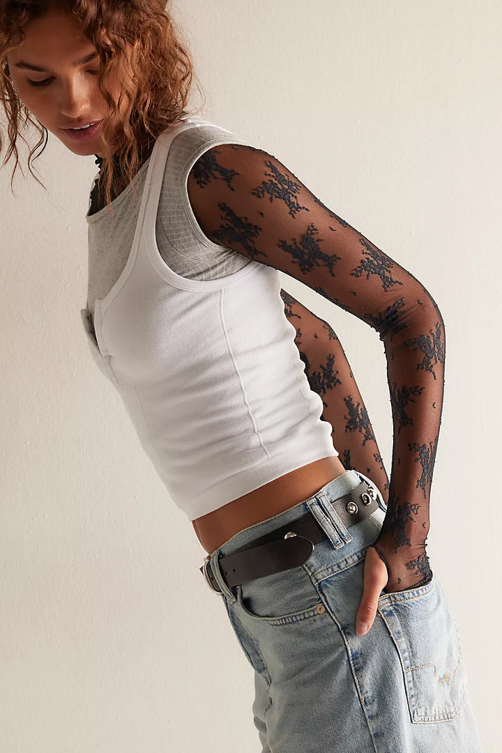 A model wearing a white ribbed tank top, light-wash denim jeans, and sheer black patterned long-sleeve tights against a plain off-white background.