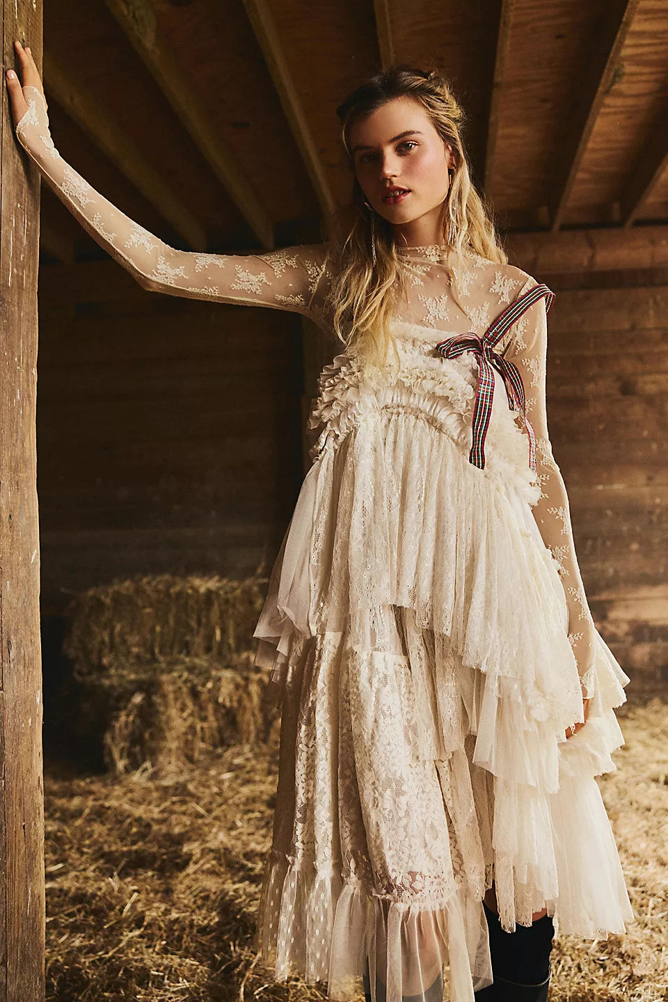 Woman in a white lace dress with a bow standing in a rustic barn.