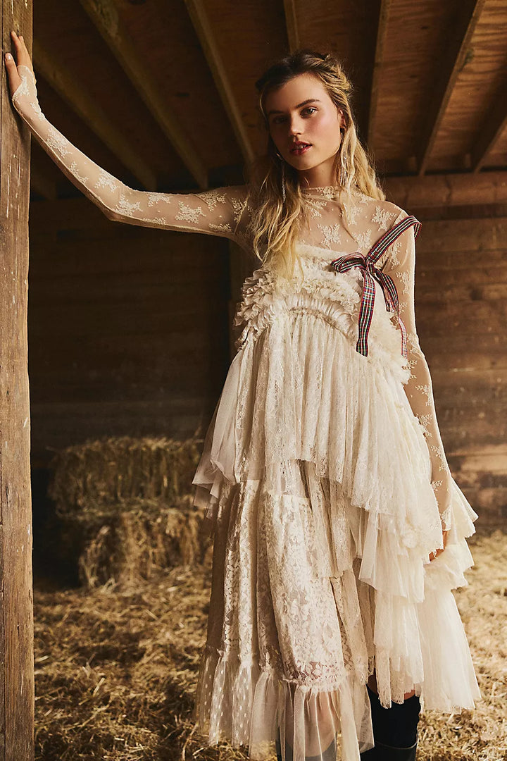 Woman in a white lace dress with a bow standing in a rustic barn.