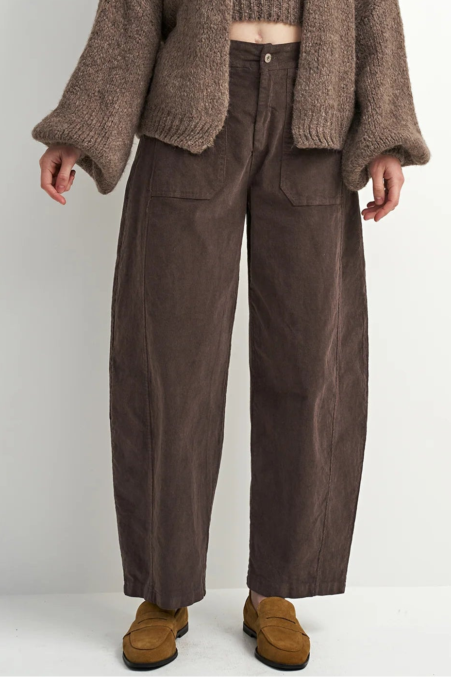 Woman wearing a brown knitted cardigan and pants against a white background