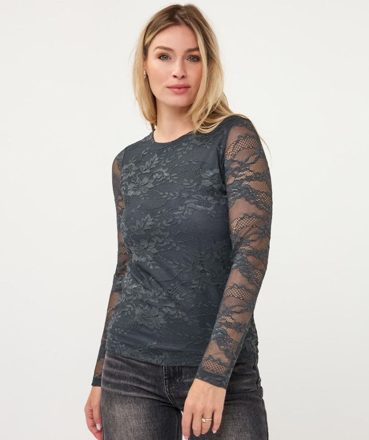 A woman modeling a dark gray long-sleeve top with a floral lace pattern and sheer sleeves, paired with dark gray jeans, against a plain white studio background.