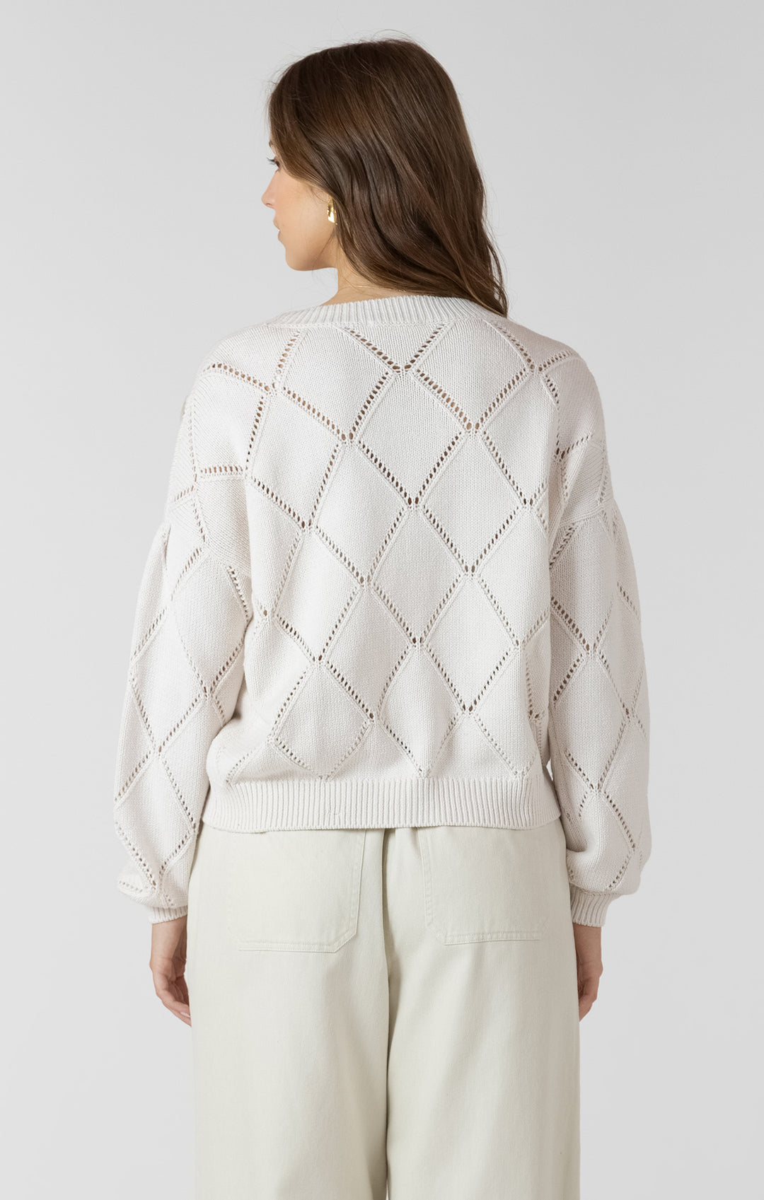 Woman wearing a light gray sweater with a diamond pattern on a white background