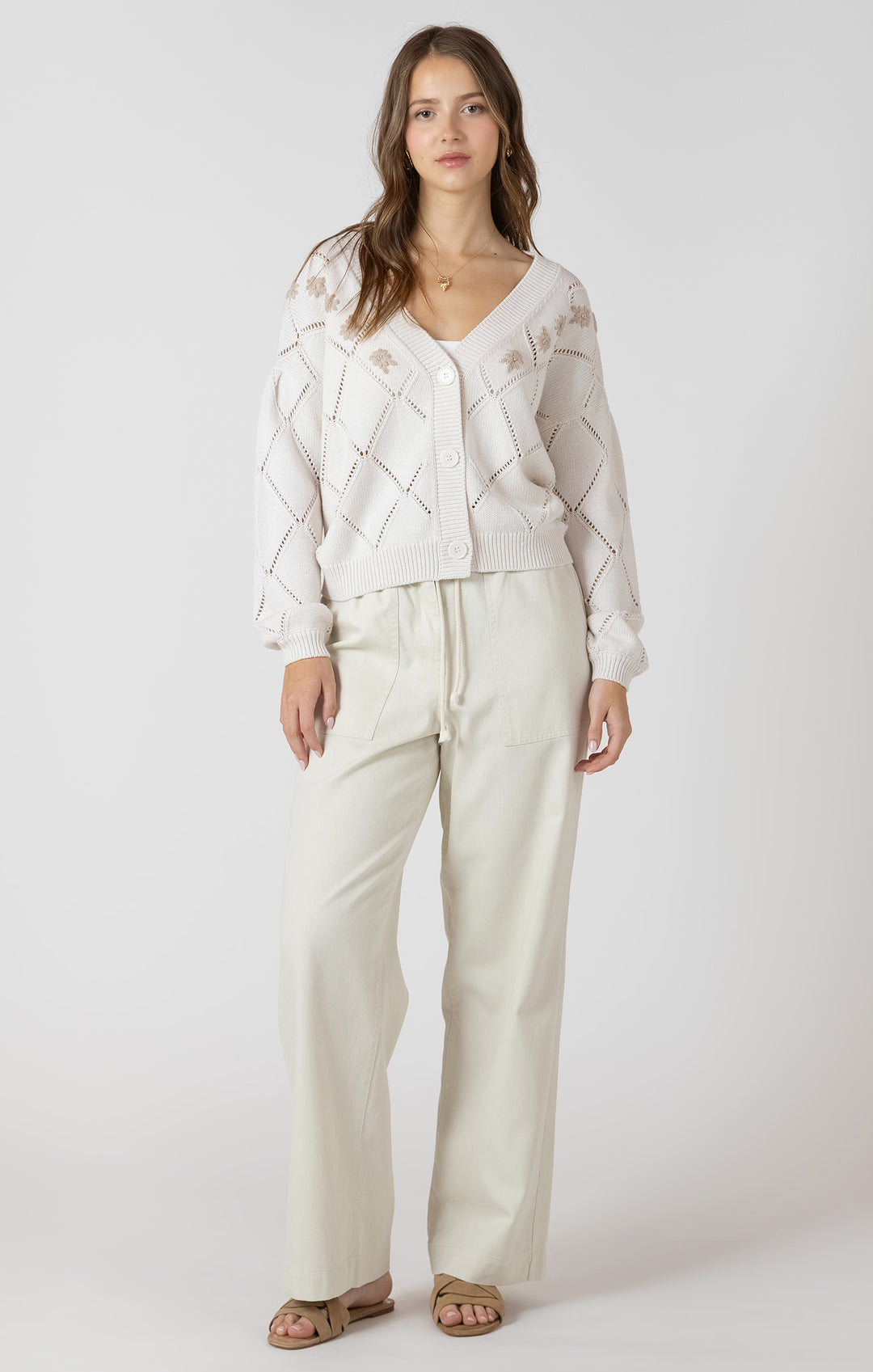 Woman wearing a white textured cardigan and pants on a white background