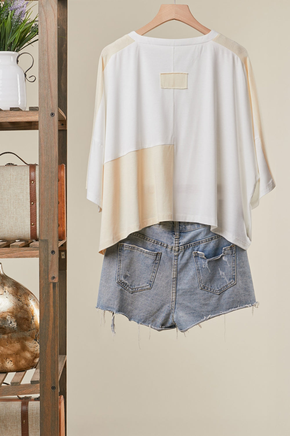 White and beige top with denim shorts on a hanger against a neutral background