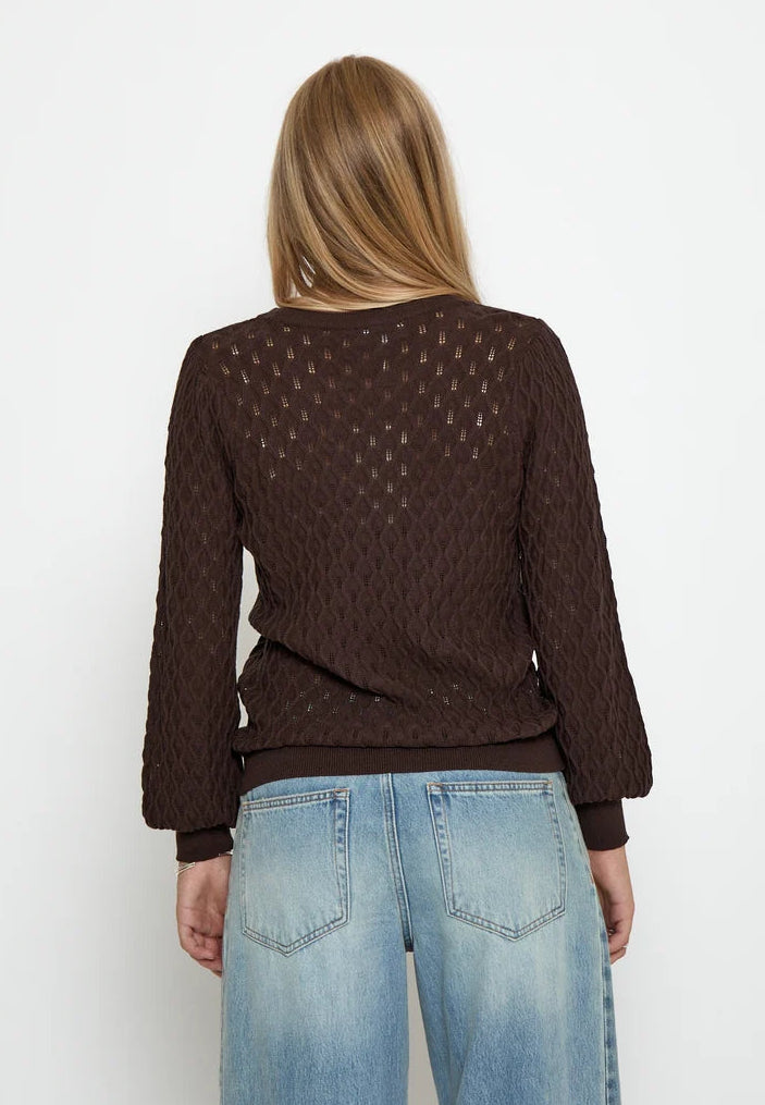 A woman viewed from the back wearing a dark brown textured knit sweater and light blue jeans against a plain white background.