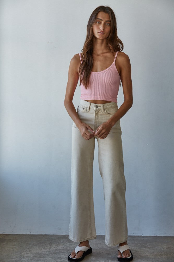 Woman wearing a pink tank top and beige pants against a plain background