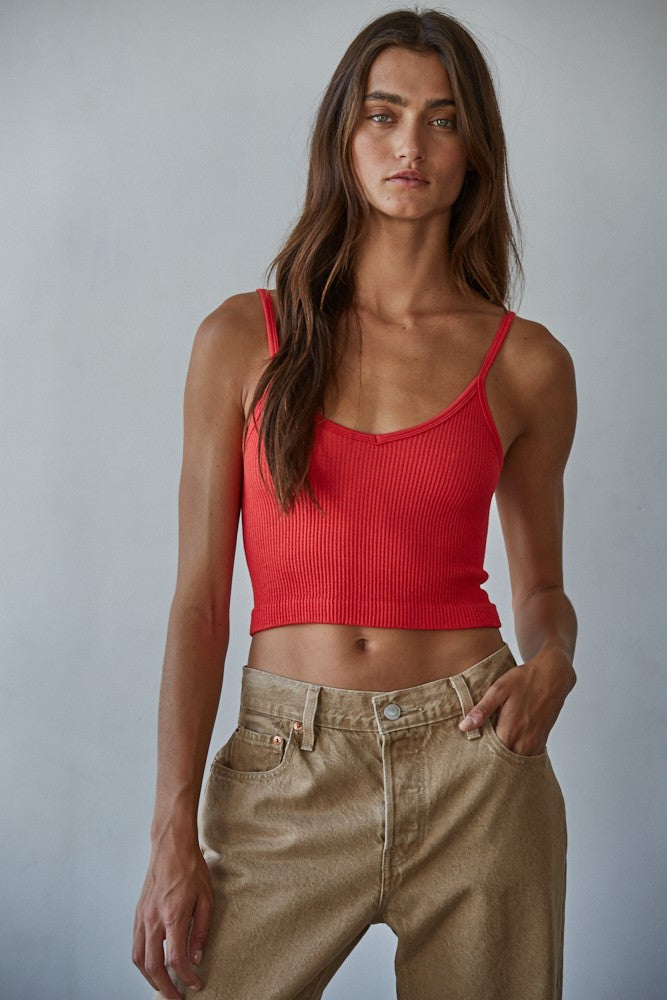 Woman wearing a red tank top and beige pants against a plain background