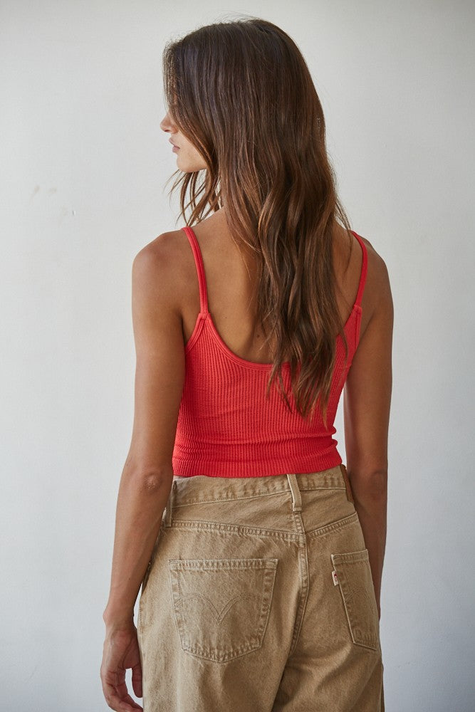 Woman wearing a red tank top and beige pants against a plain background