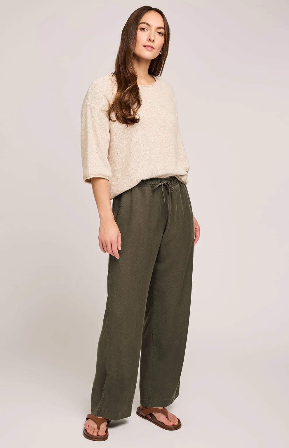 Woman wearing a beige top and green pants on a white background