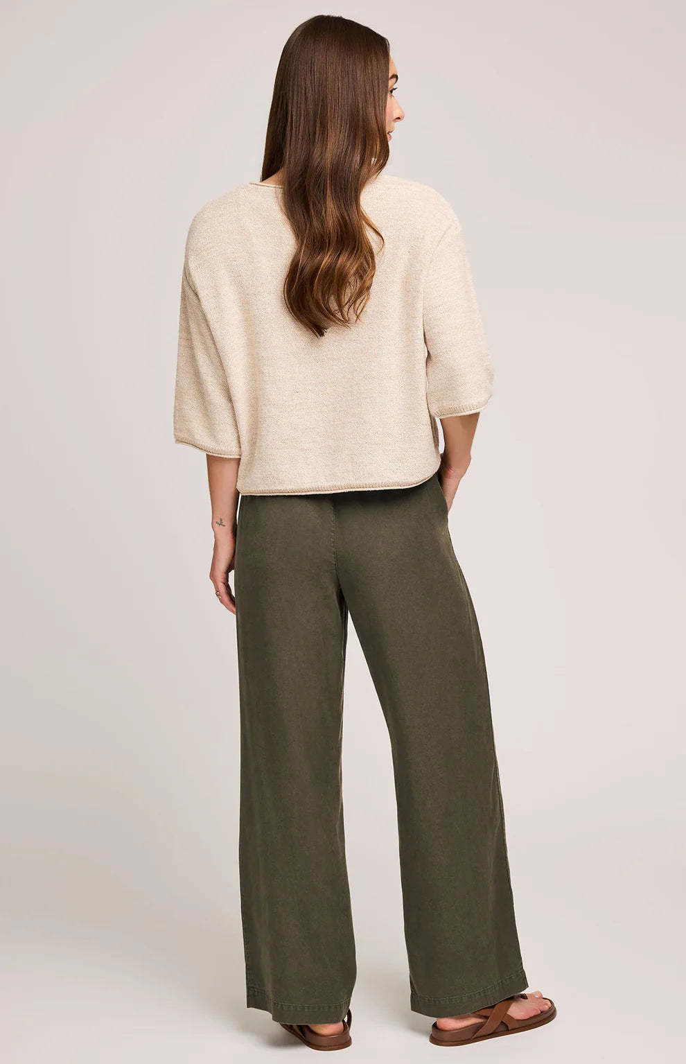 Woman wearing a beige top and green pants on a plain background