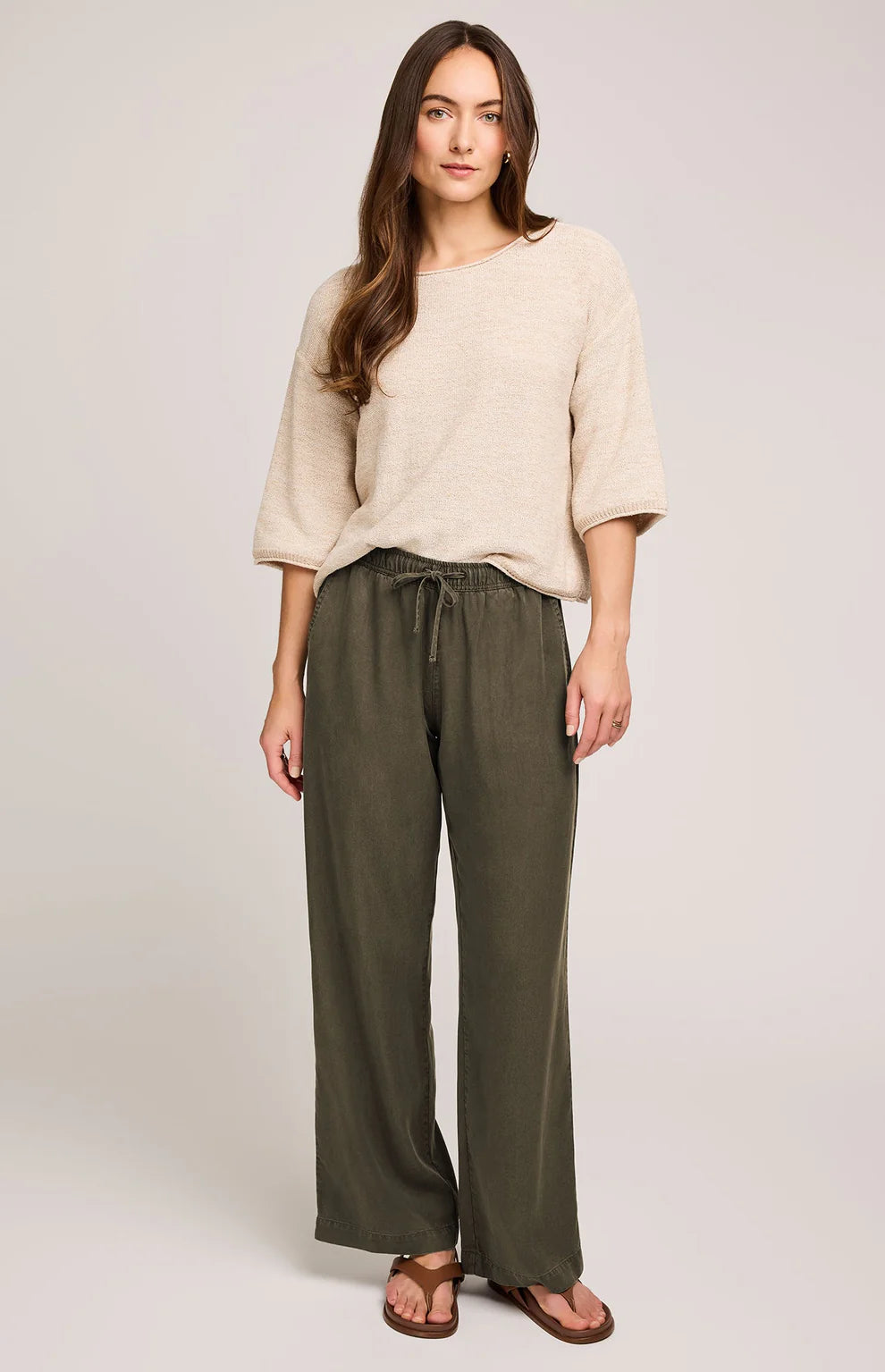 Woman wearing a beige top and olive green pants on a plain background