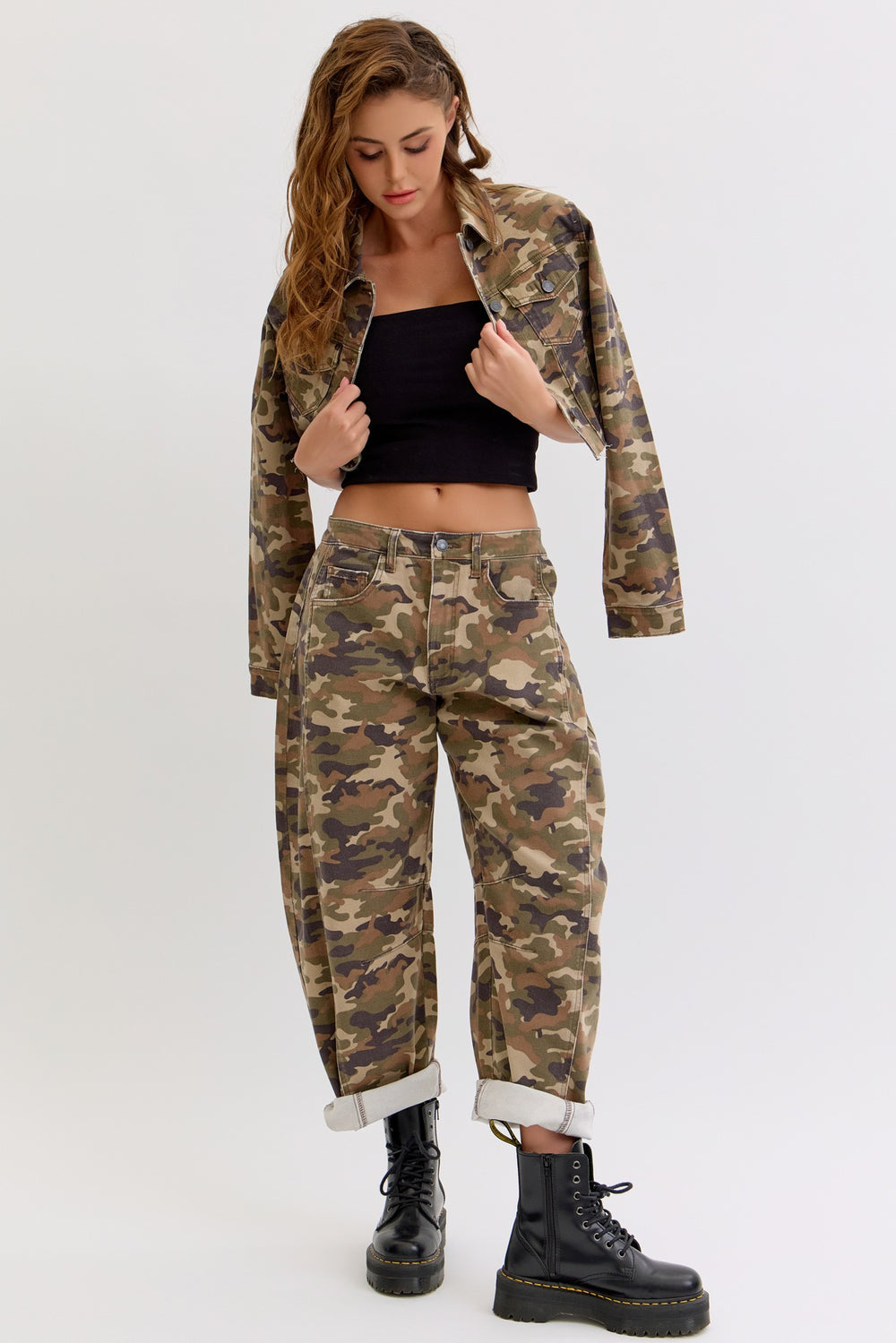 Woman wearing a camouflage jacket and pants with black boots on a white background