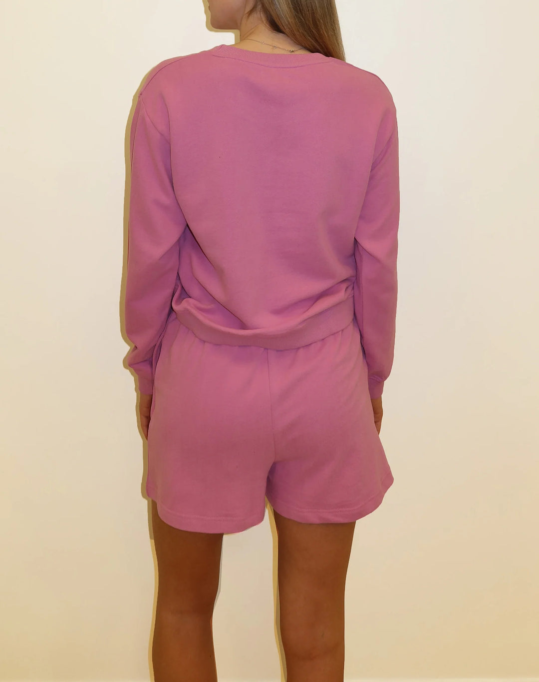 Person wearing a pink long-sleeve top and shorts set against a beige background