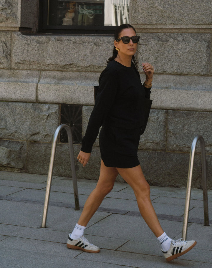 Woman in a black outfit walking on a sidewalk with a stone building in the background