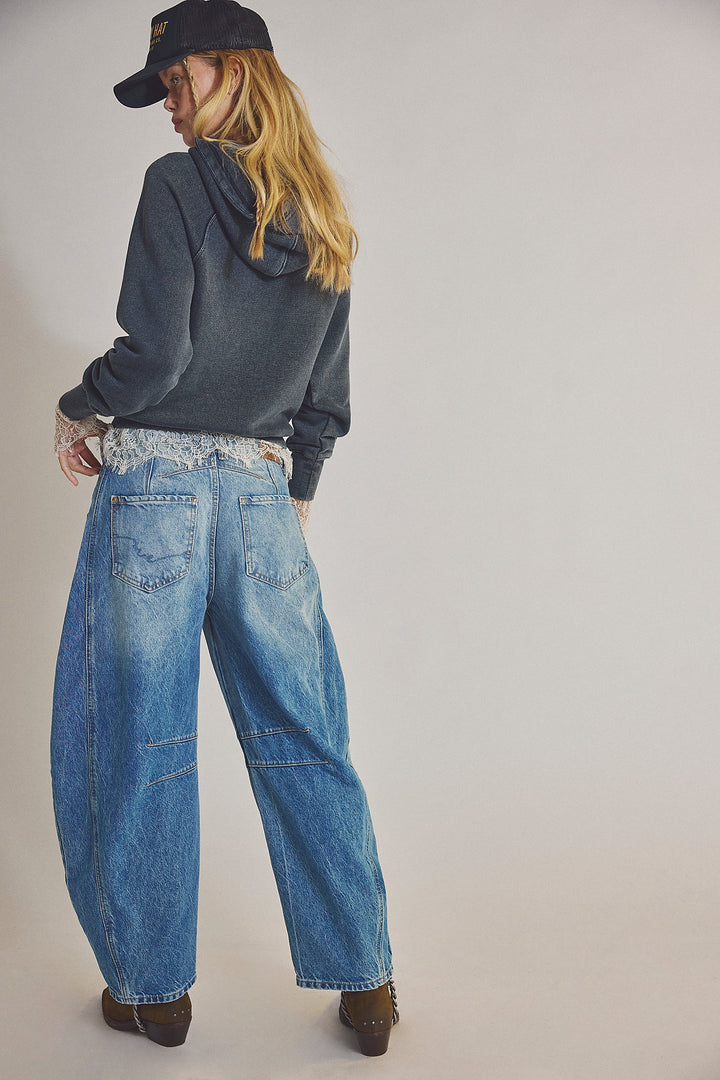 Person wearing a dark hoodie and blue jeans on a plain background
