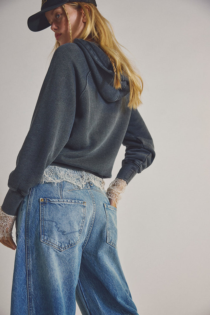 Person wearing a dark hoodie and blue jeans with lace details on a plain background
