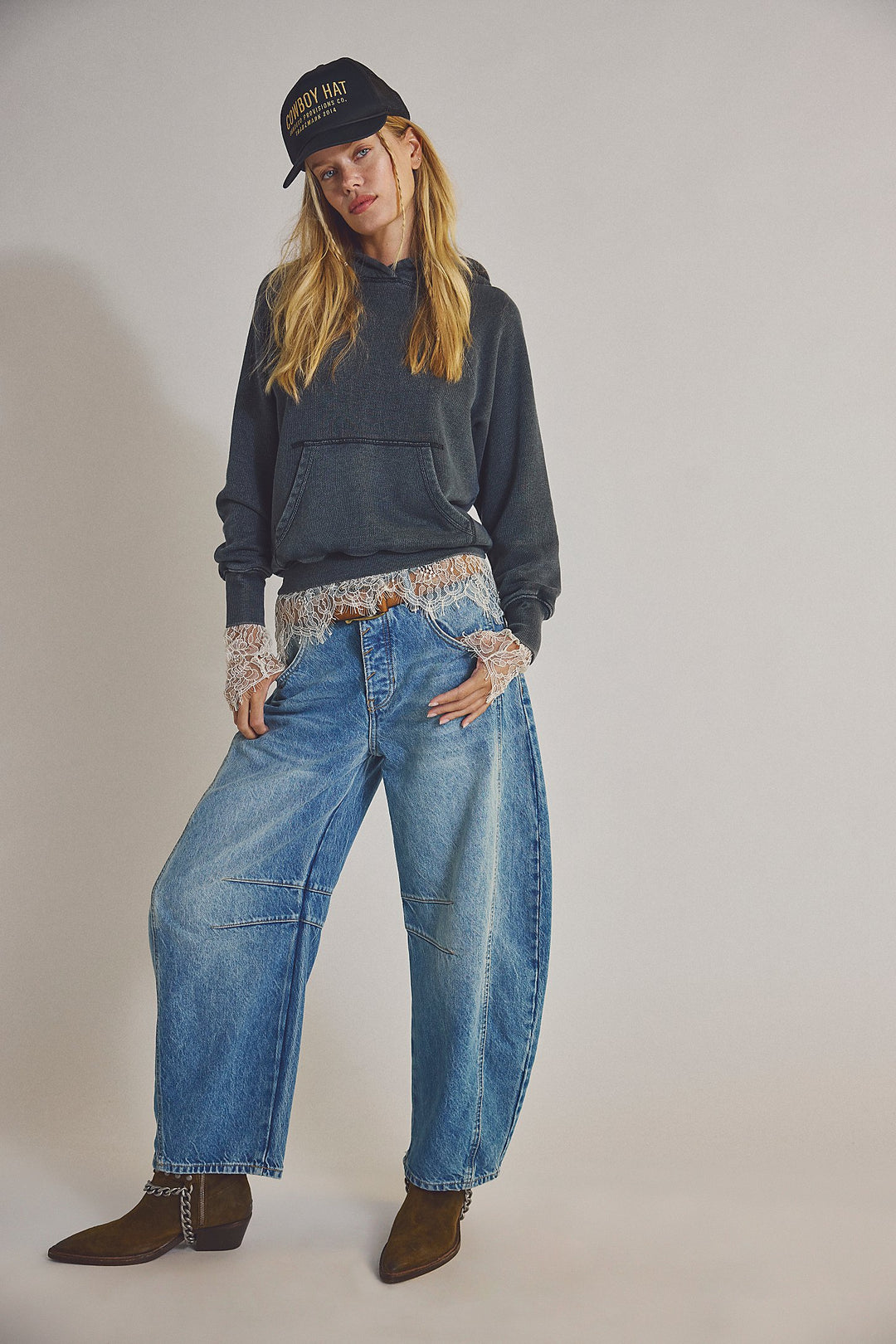 Person wearing a dark sweater, patterned leggings, blue jeans, and a cap on a plain background