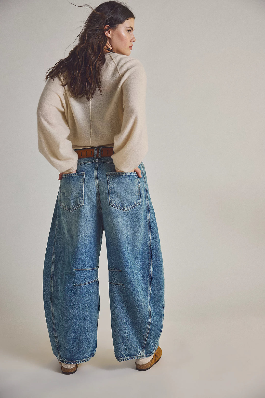 Woman wearing a beige sweater and blue jeans on a plain background