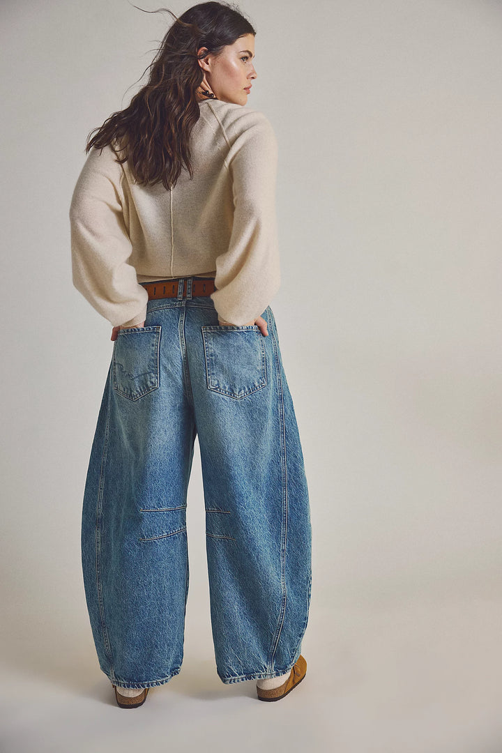 Woman wearing a beige sweater and blue jeans on a plain background