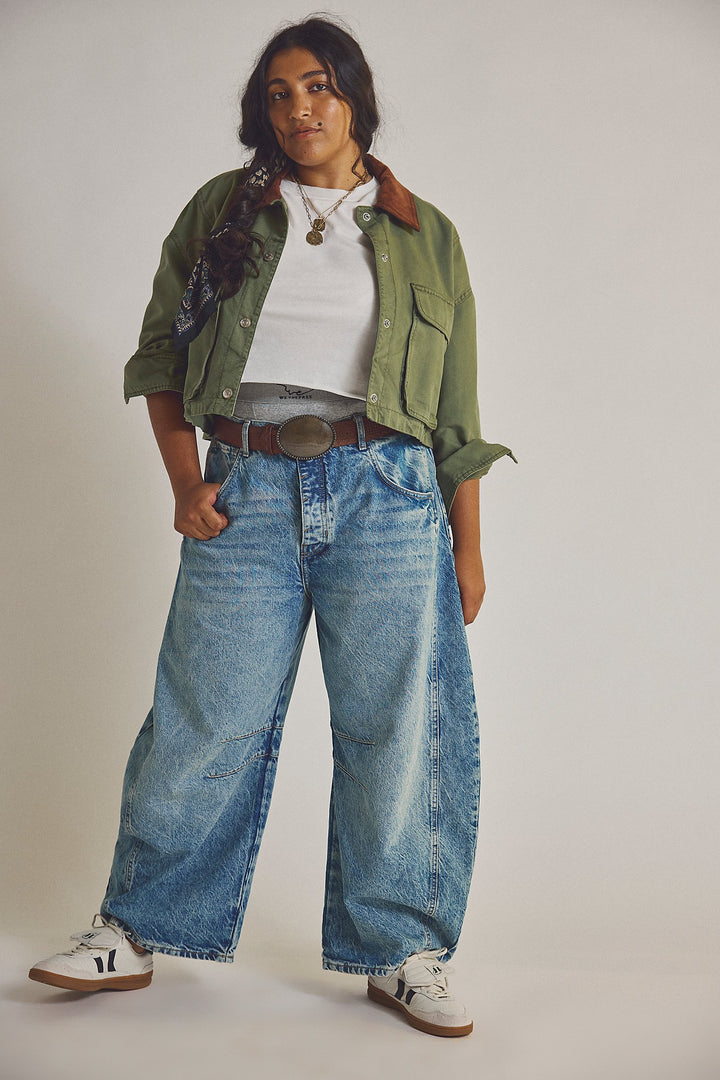 Person wearing a green jacket, white shirt, and blue jeans on a plain background