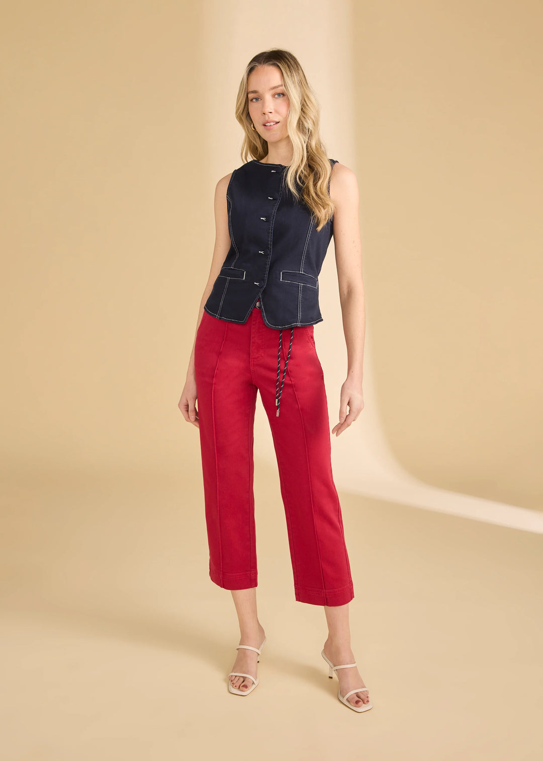 Woman wearing a black sleeveless jacket and red pants on a beige background