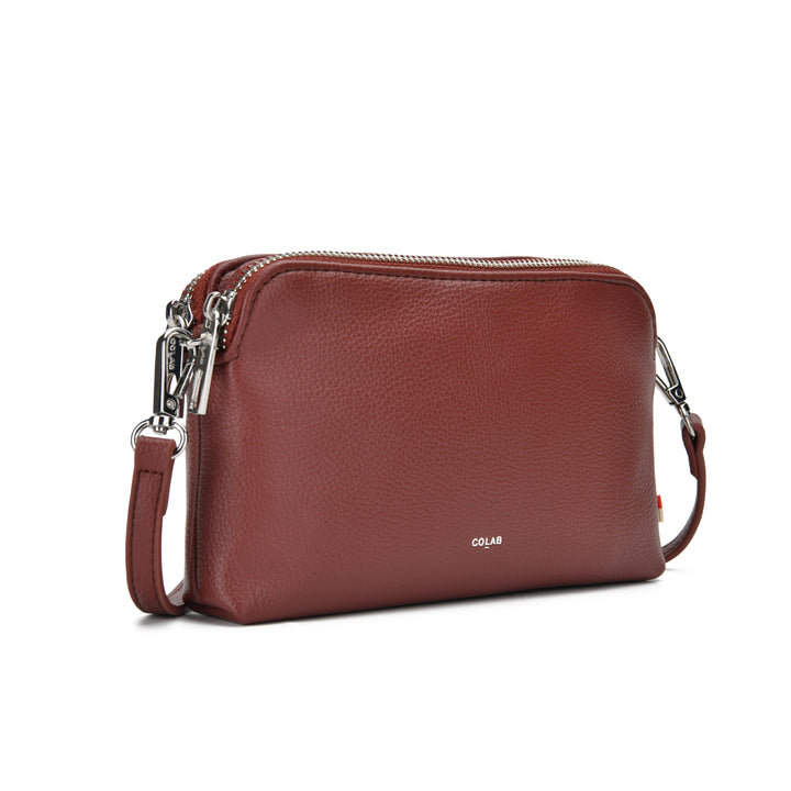 A reddish-brown pebbled leather crossbody bag with silver-tone hardware and a small white COLAB logo on the front, shown on a clean white background.