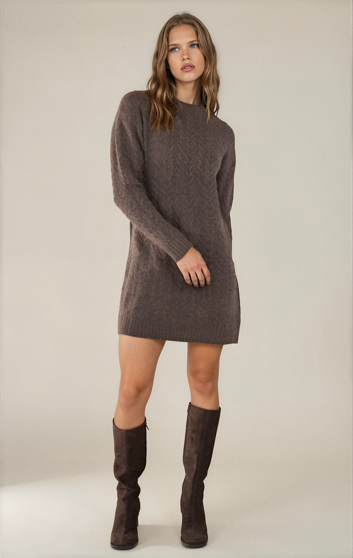 A woman modeling a brown cable-knit sweater dress with long sleeves, paired with matching brown knee-high boots, against a neutral studio background.