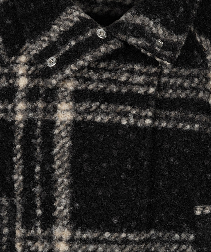 Close-up of a dark plaid wool or wool-blend shirt jacket with a collar, silver-toned buttons, and a textured woven pattern in black and off-white.