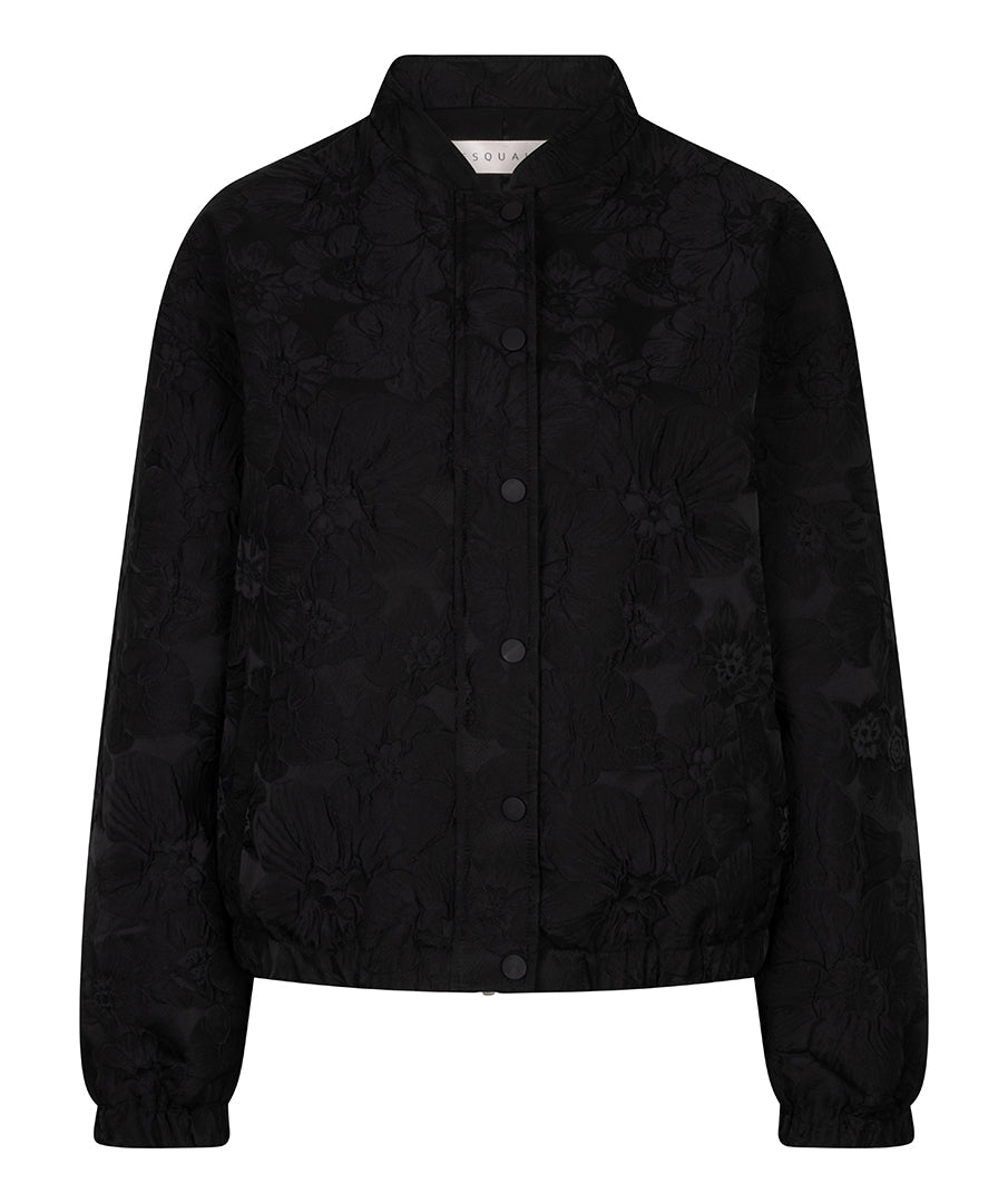 A black cropped jacket with a subtle tonal floral jacquard pattern, featuring a stand collar, button-front closure, and elasticized cuffs and hem, shown against a plain white background.
