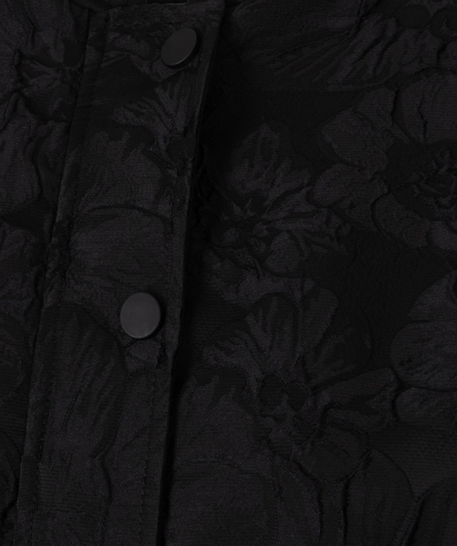 Close-up of a black textured fabric with an embossed floral pattern and dark buttons on a placket.