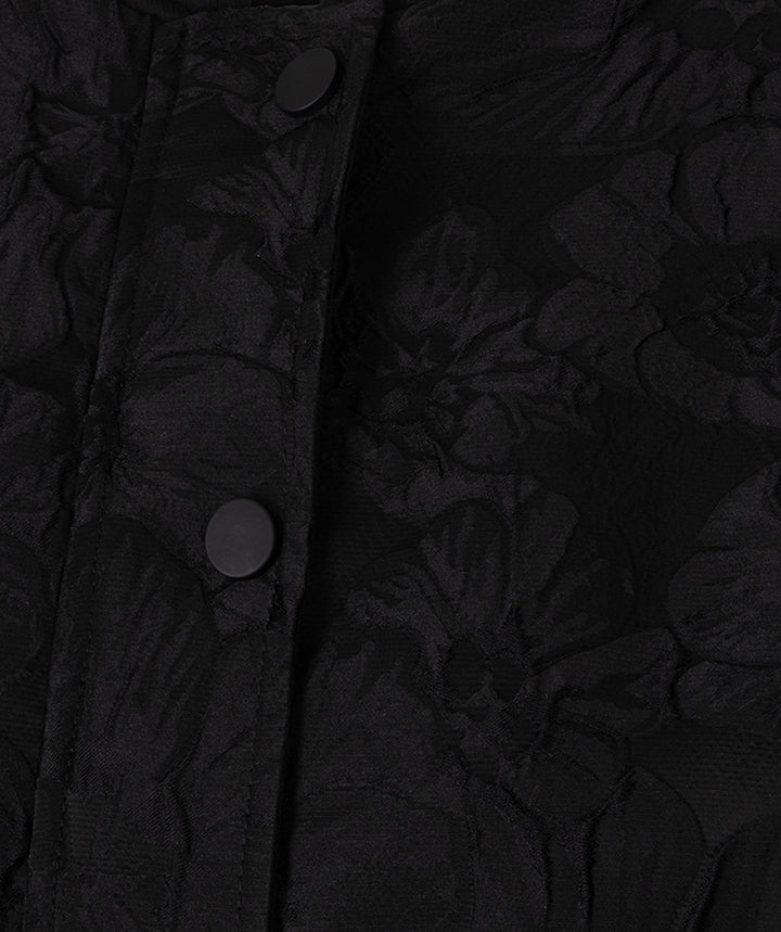 Close-up of a black textured fabric with an embossed floral pattern and dark buttons on a placket.