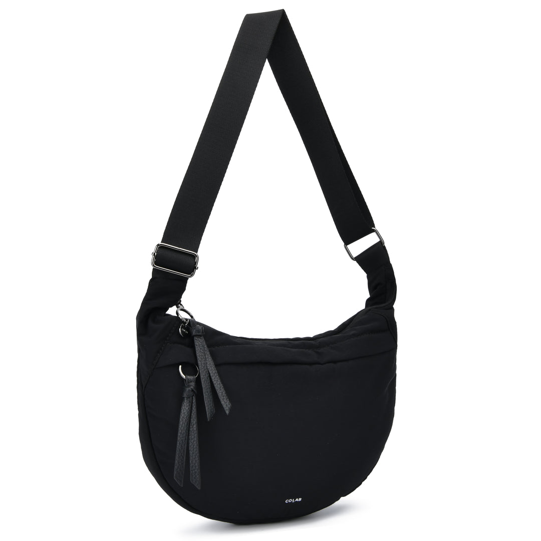 A black nylon shoulder bag with an adjustable webbing strap, a front zippered pocket with leather tassel pulls, and a small white &