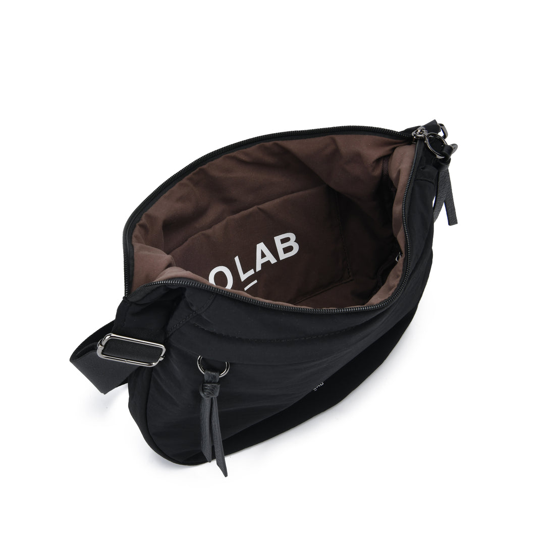 A black nylon crossbody bag shown open from an overhead angle, revealing a brown interior lining with the brand name &