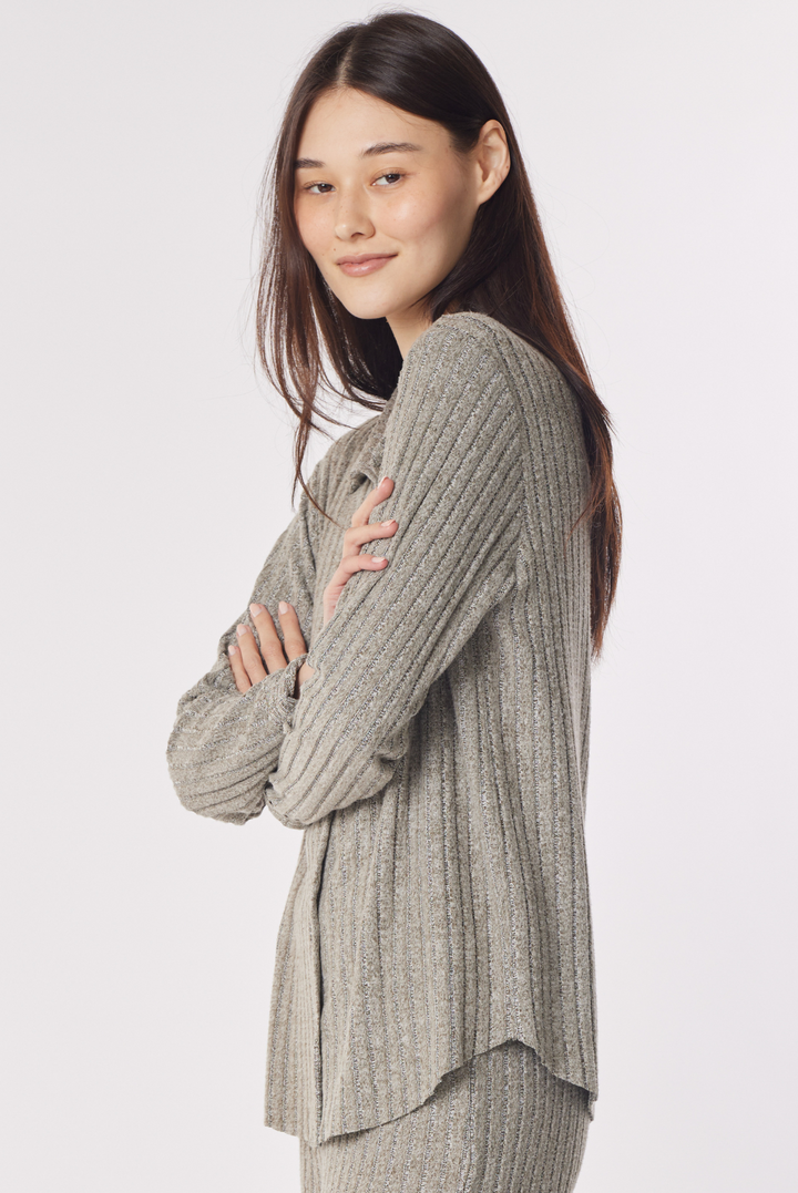 A woman modeling a ribbed knit matching set consisting of a light gray long-sleeve top and coordinating pants against a plain light gray studio background.