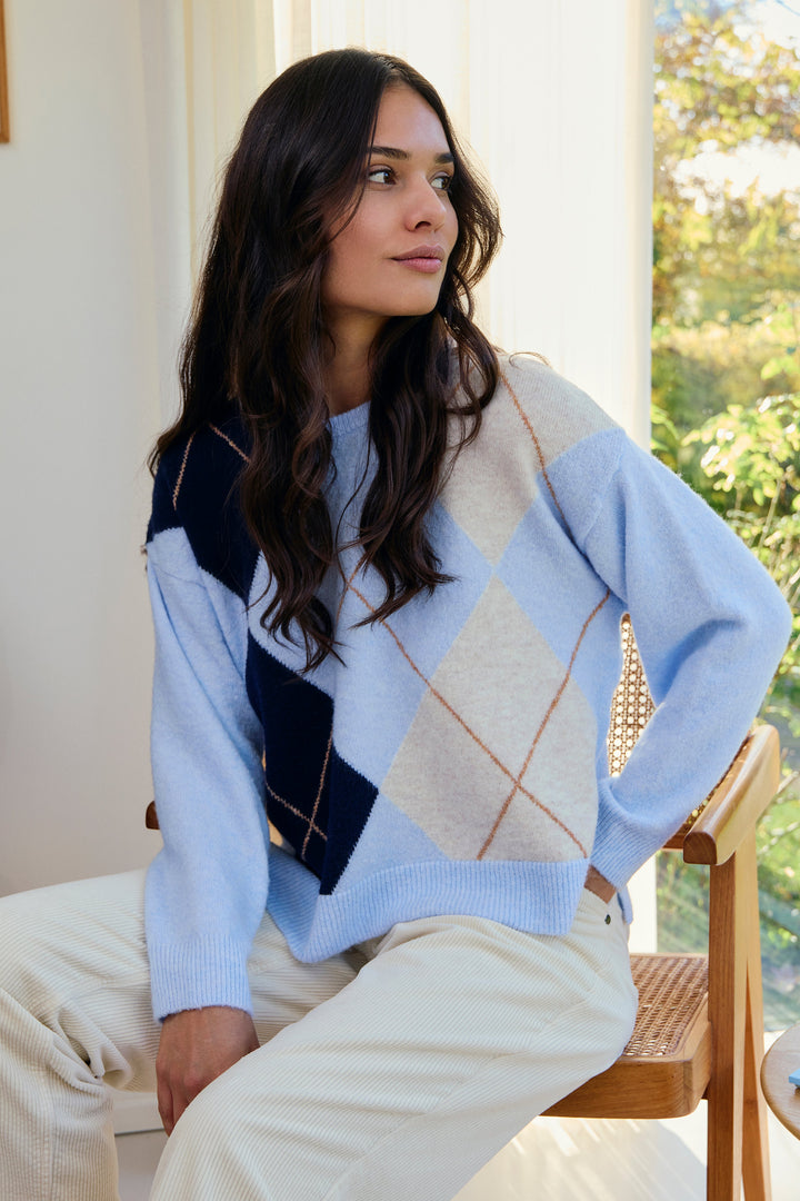 Woman sitting on a chair wearing a colorful sweater in a bright room with a window.