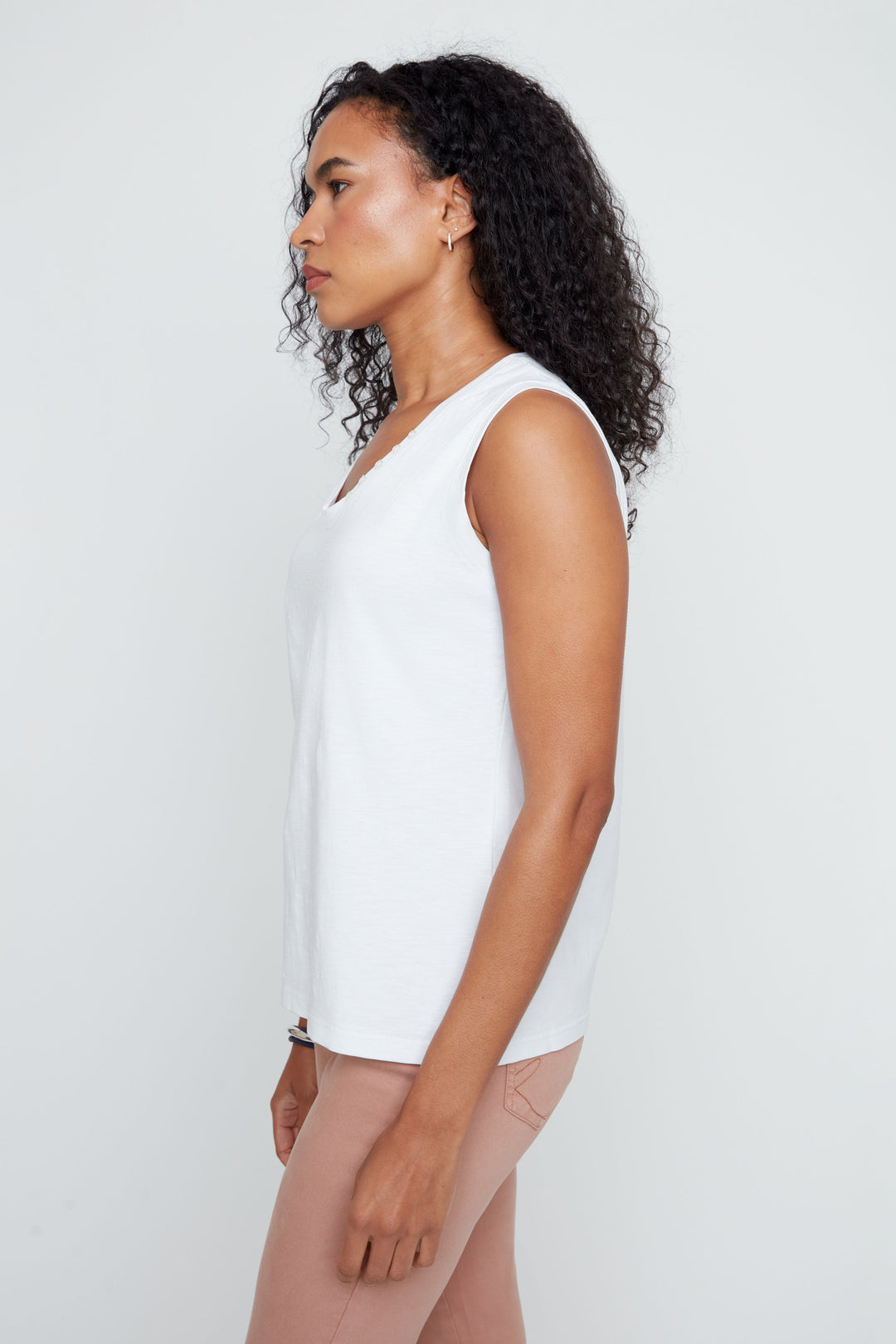 Woman wearing a white sleeveless top against a plain background