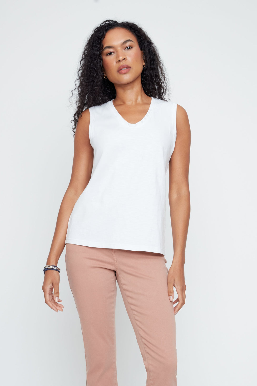 Woman wearing a white sleeveless top and pink pants with lace details on a white background