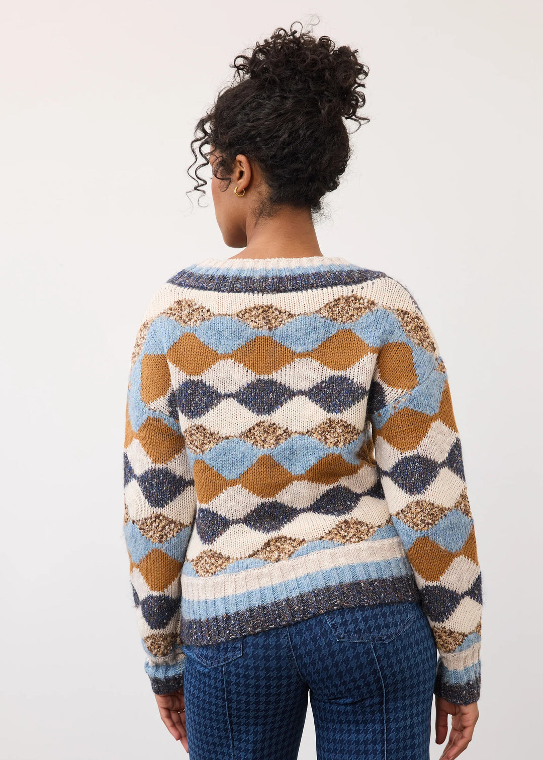 A woman shown from the back wearing a long-sleeve knit sweater with a geometric diamond pattern in cream, light blue, mustard brown, and navy, paired with blue houndstooth pants against a plain white studio background.