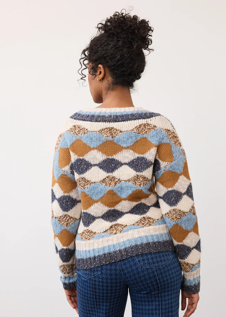 A woman shown from the back wearing a long-sleeve knit sweater with a geometric diamond pattern in cream, light blue, mustard brown, and navy, paired with blue houndstooth pants against a plain white studio background.