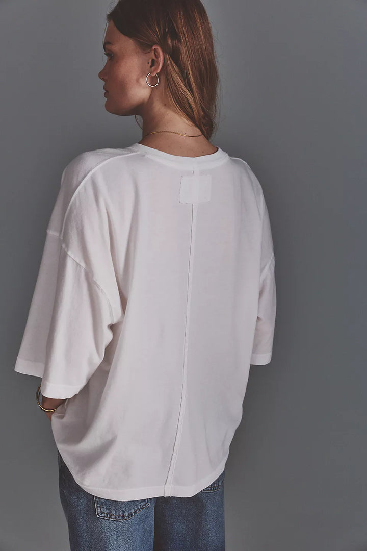 A woman shown from the back wearing an oversized white top and blue jeans against a plain gray studio background.