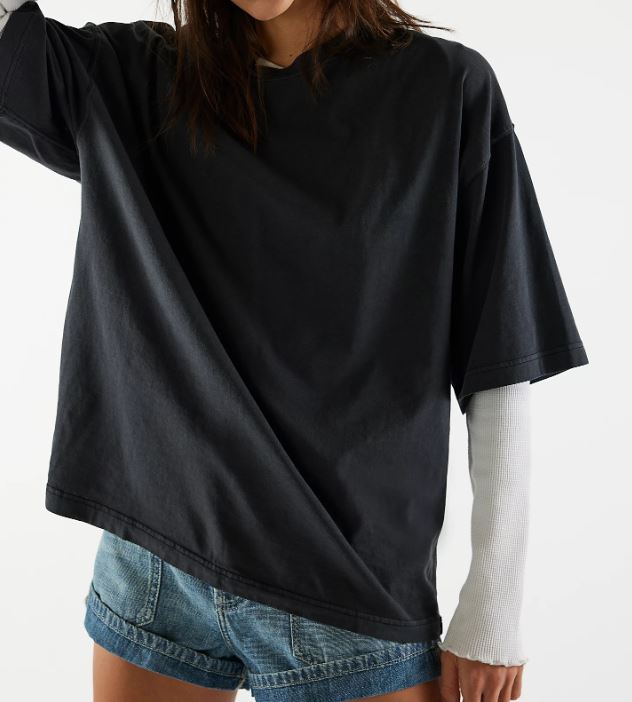 A person wearing an oversized black short-sleeve t-shirt layered over a white ribbed long-sleeve shirt and blue denim shorts, shown against a plain white background.